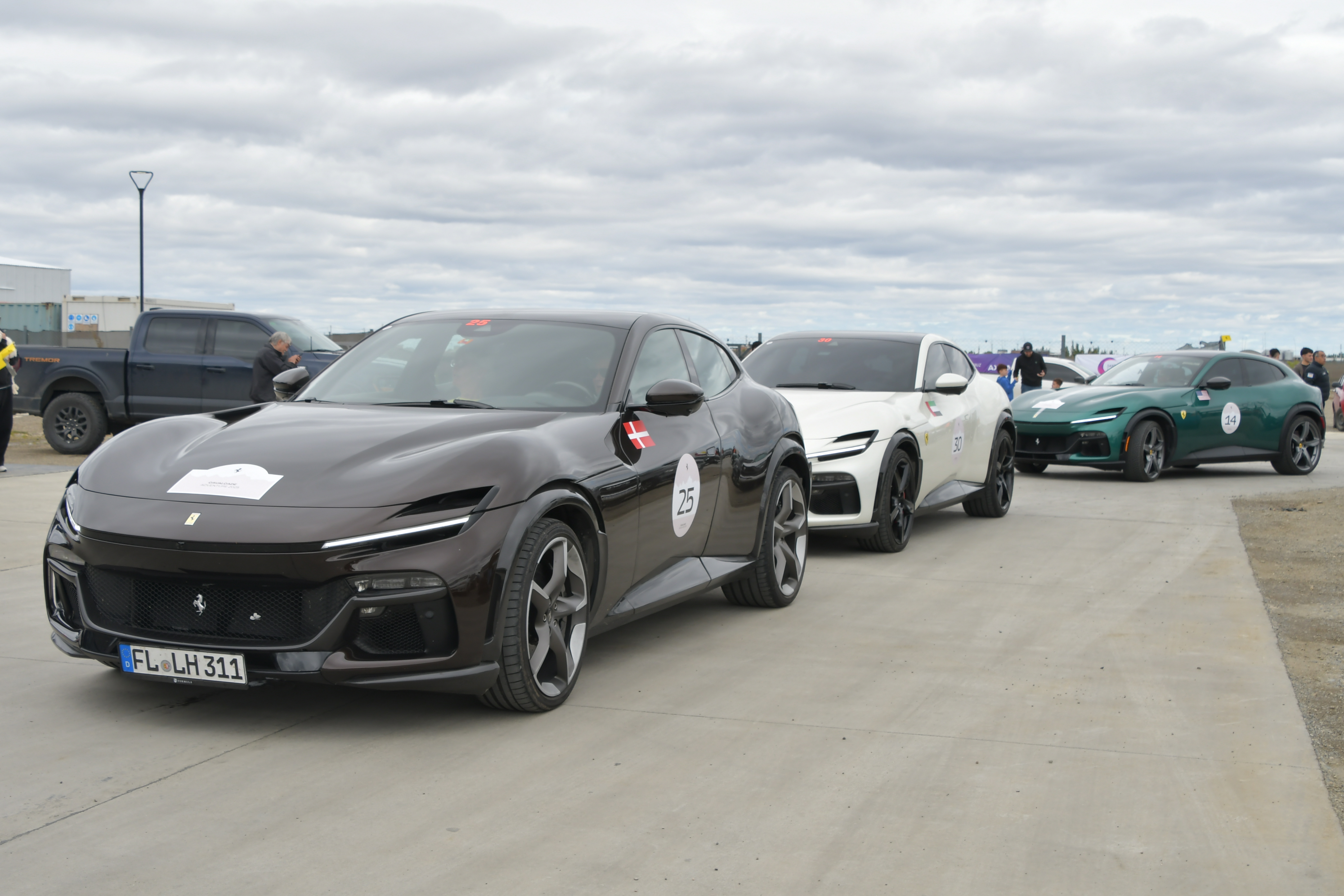  Una Ferrari encabeza la caravana al ingresar a la estación de servicio frente a la gente que observa desde la vereda. FOTO: JUAN PALACIOS / LA OPINIÓN AUSTRAL.